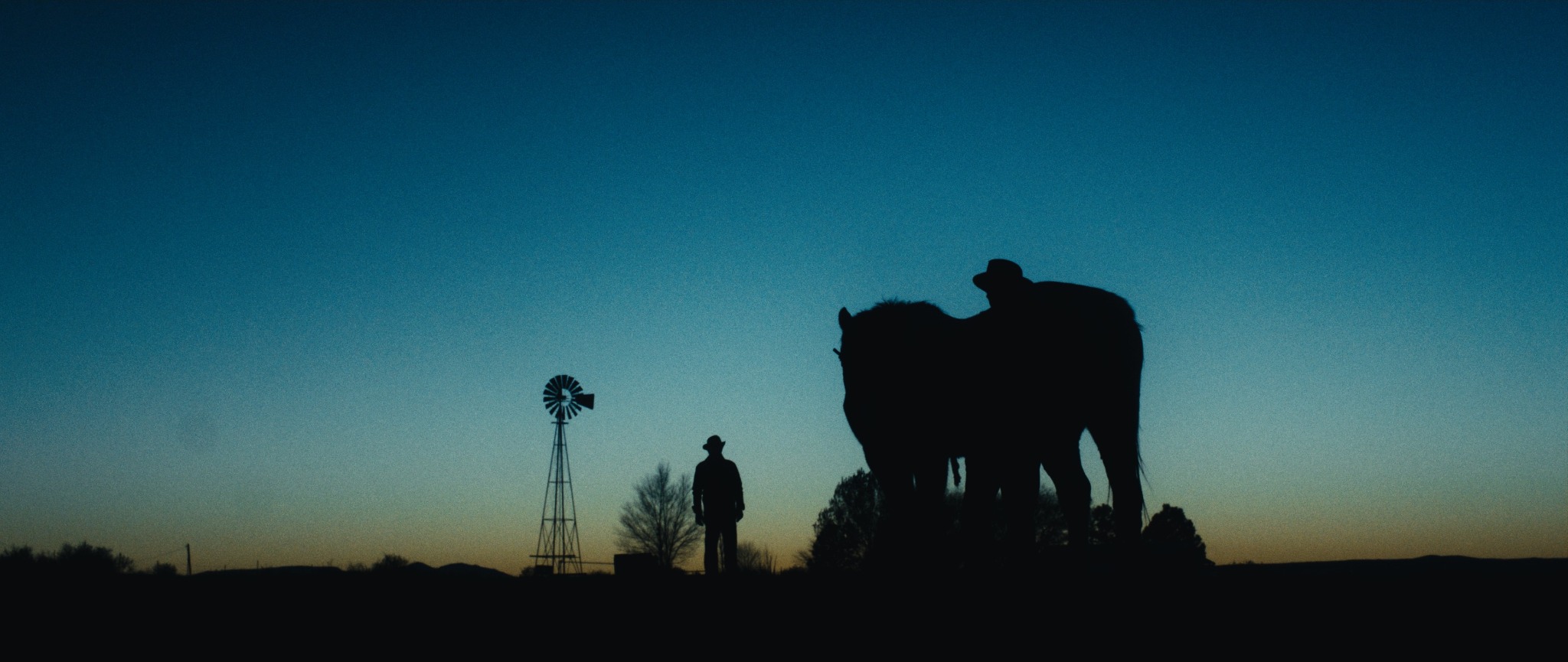 Rivals still: a horse and rider, standing figure, and windmill silhouetted at dusk